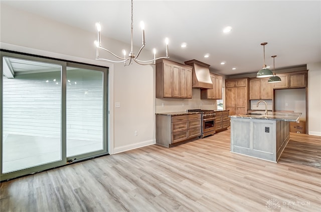 kitchen with pendant lighting, custom exhaust hood, stainless steel stove, light wood-type flooring, and light stone counters