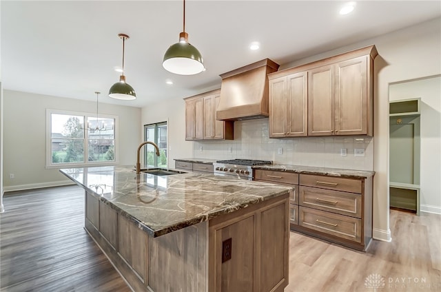 kitchen featuring sink, an island with sink, pendant lighting, and custom range hood