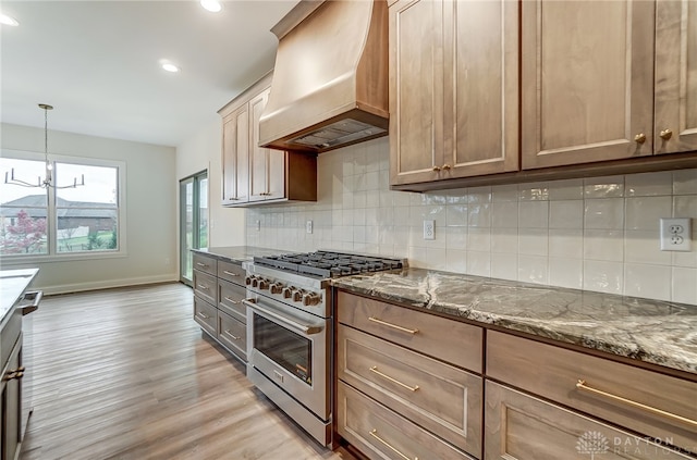 kitchen featuring stone counters, light hardwood / wood-style flooring, premium range hood, backsplash, and high end stainless steel range