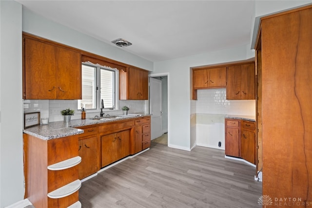 kitchen featuring light stone counters, light hardwood / wood-style flooring, backsplash, and sink