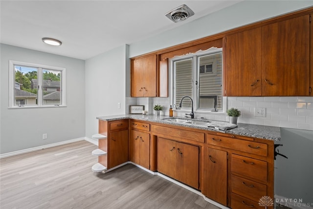 kitchen with stone countertops, sink, decorative backsplash, and light hardwood / wood-style floors