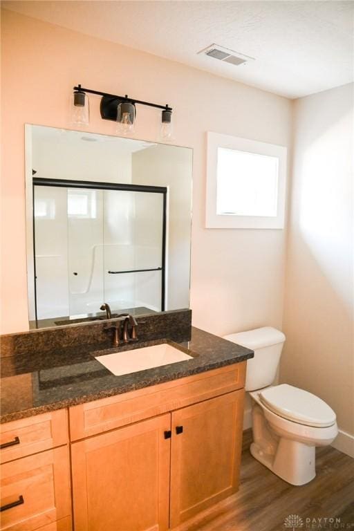 bathroom featuring visible vents, an enclosed shower, wood finished floors, vanity, and toilet
