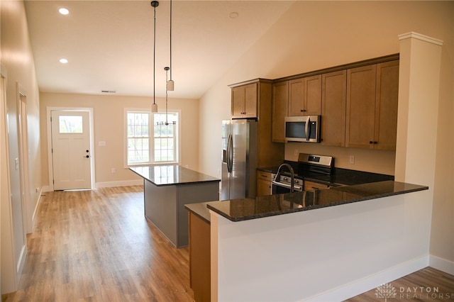 kitchen featuring lofted ceiling, light hardwood / wood-style flooring, stainless steel appliances, dark stone countertops, and pendant lighting