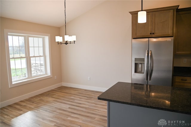 kitchen featuring hanging light fixtures, stainless steel fridge with ice dispenser, vaulted ceiling, light hardwood / wood-style flooring, and dark stone countertops