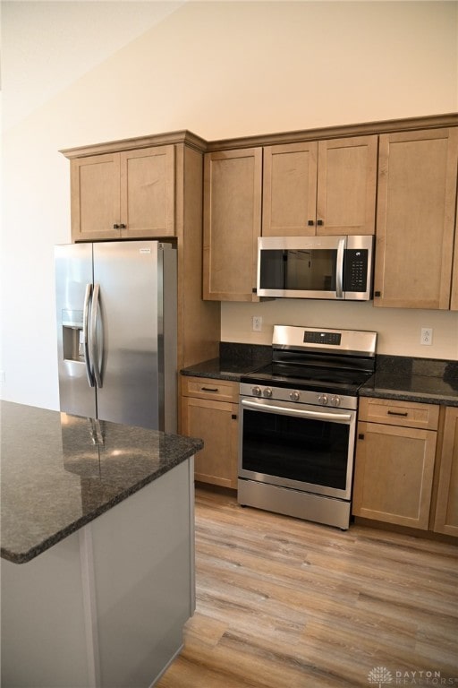 kitchen with lofted ceiling, stainless steel appliances, light wood-type flooring, and dark stone countertops