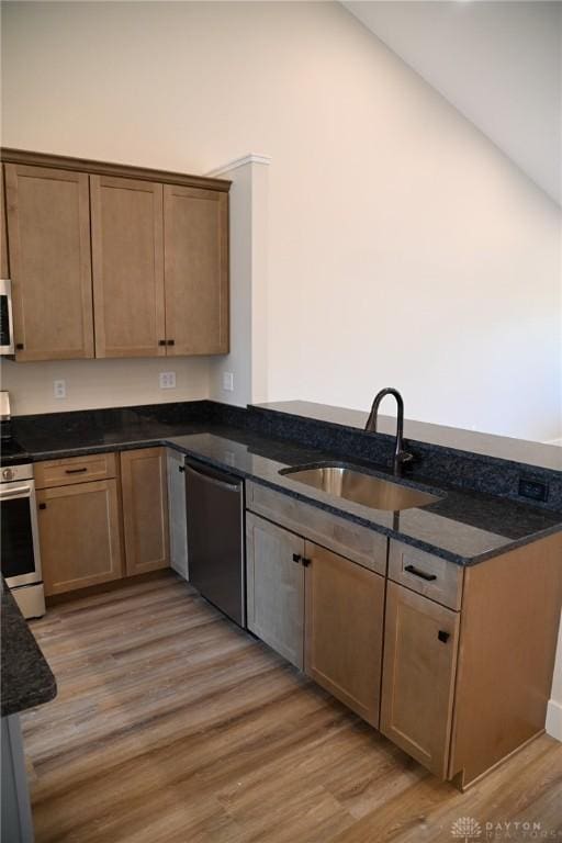 kitchen with appliances with stainless steel finishes, a sink, a peninsula, light wood finished floors, and dark stone counters