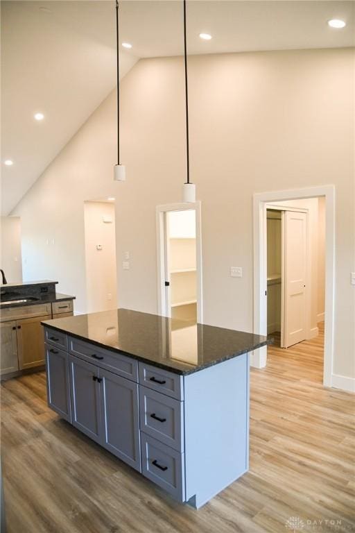 kitchen featuring dark stone counters, high vaulted ceiling, a sink, and light wood-style flooring