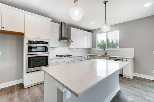 kitchen with white cabinetry, sink, pendant lighting, and wall chimney exhaust hood