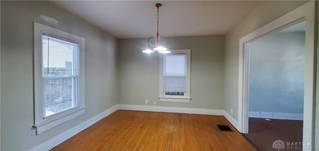 unfurnished dining area with an inviting chandelier and hardwood / wood-style flooring