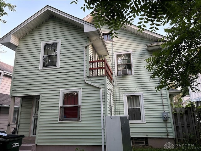 rear view of house featuring cooling unit, fence, and a balcony