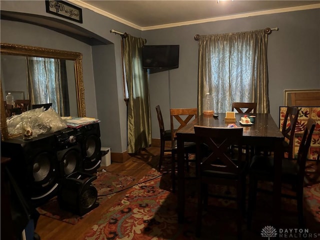 dining space featuring arched walkways, crown molding, and wood finished floors