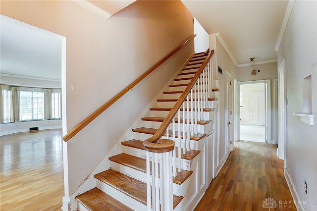 stairway with wood-type flooring and ornamental molding