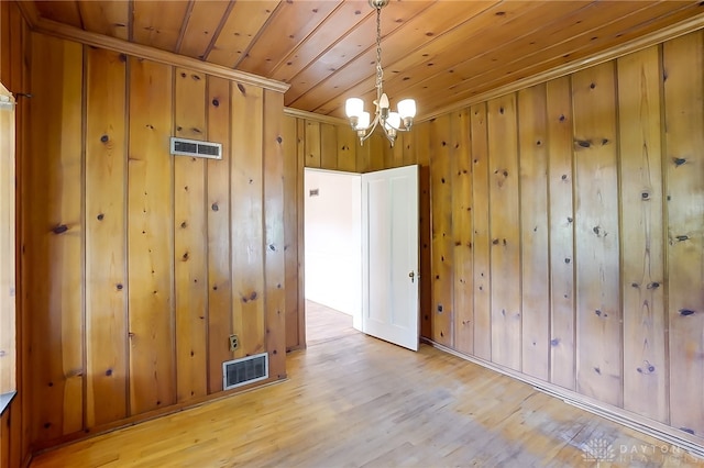 empty room featuring crown molding, a chandelier, light wood-type flooring, wood walls, and wooden ceiling