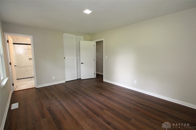 unfurnished bedroom featuring ensuite bath and dark hardwood / wood-style flooring