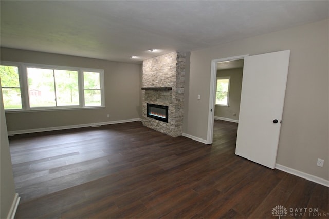 unfurnished living room featuring a stone fireplace and dark wood-type flooring