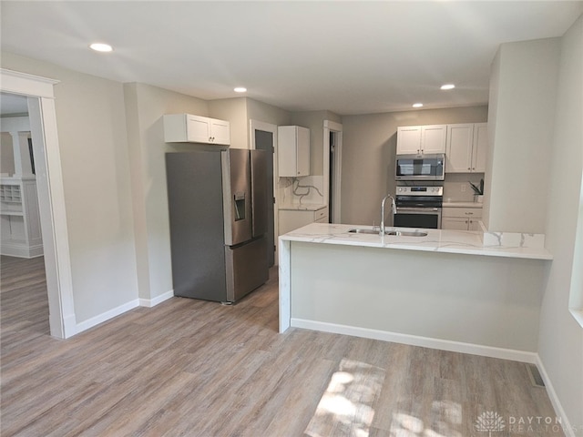 kitchen with kitchen peninsula, appliances with stainless steel finishes, white cabinetry, light hardwood / wood-style flooring, and sink