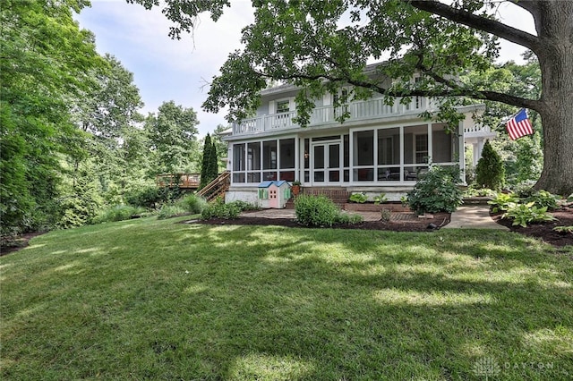 back of property featuring a yard, a balcony, and a sunroom