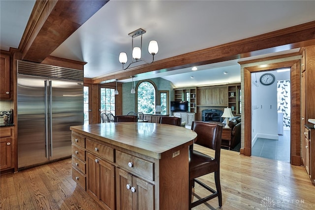 kitchen featuring wood counters, a kitchen breakfast bar, pendant lighting, a center island, and built in fridge