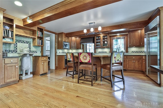 kitchen featuring backsplash, a kitchen breakfast bar, wall chimney range hood, built in appliances, and light wood-type flooring