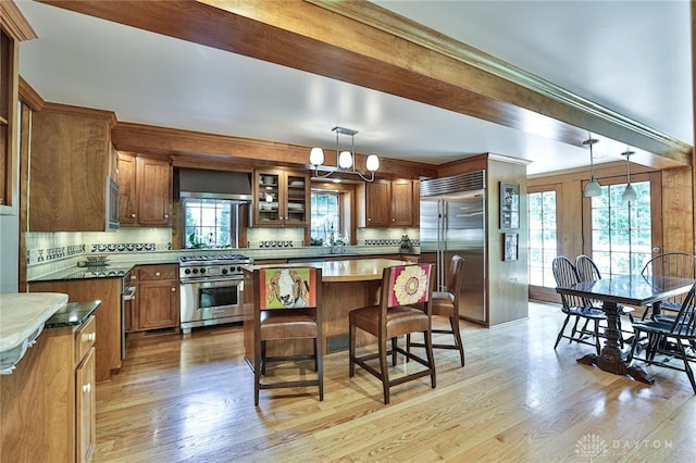 kitchen with built in appliances, pendant lighting, wall chimney range hood, and tasteful backsplash