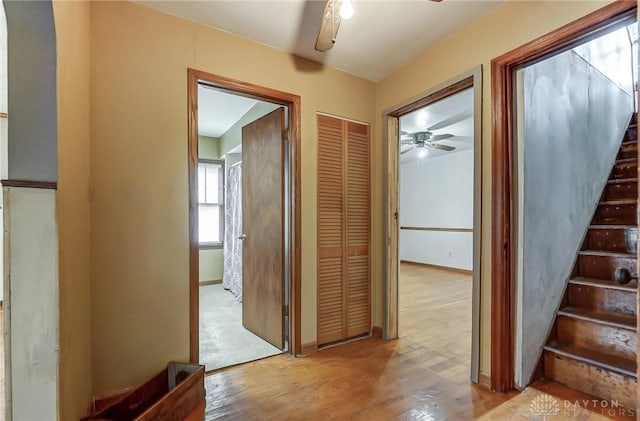 hallway with baseboards, light wood finished floors, and stairs