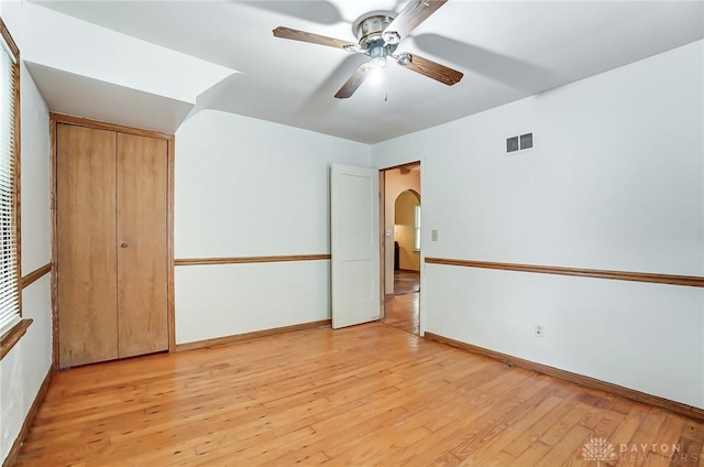 spare room with light wood finished floors, visible vents, arched walkways, and ceiling fan