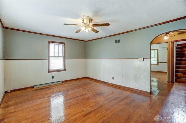 spare room with arched walkways, wainscoting, a baseboard radiator, ceiling fan, and wood finished floors