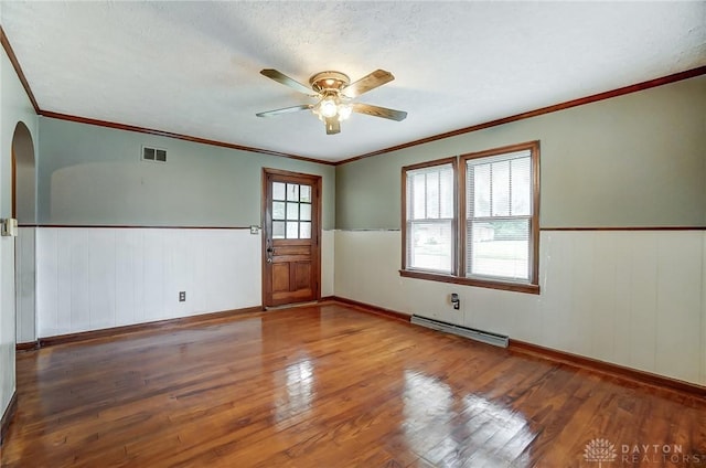 empty room featuring baseboard heating, wainscoting, wood finished floors, and visible vents