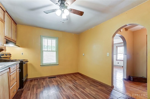 kitchen with arched walkways, electric range oven, dark countertops, dark wood-type flooring, and under cabinet range hood