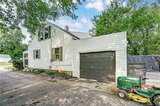 view of side of property featuring an attached garage, dirt driveway, a chimney, and fence