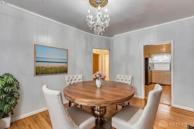 dining room with a notable chandelier, crown molding, and light wood-type flooring