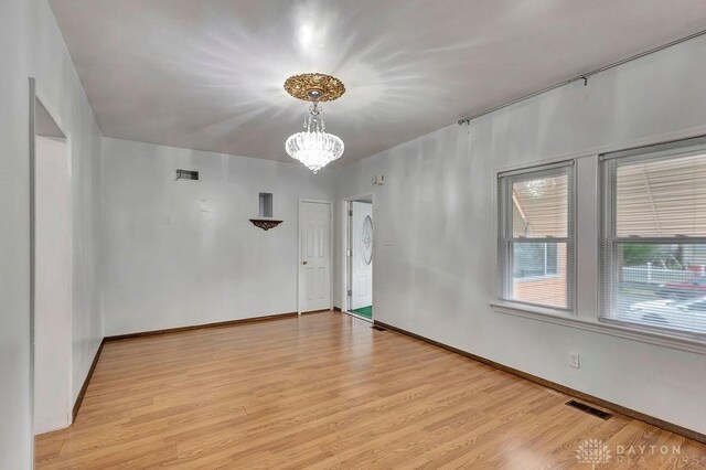 unfurnished room featuring a chandelier and light wood-type flooring