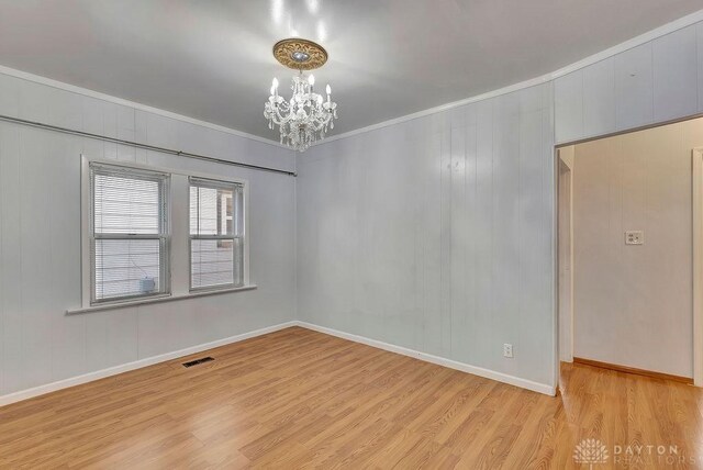 spare room with a notable chandelier, crown molding, and light wood-type flooring