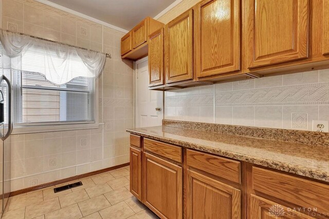 kitchen with light tile patterned floors, backsplash, tile walls, light stone countertops, and ornamental molding