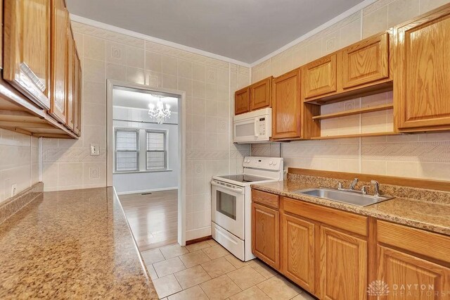 kitchen with white appliances, light wood-type flooring, an inviting chandelier, tile walls, and sink