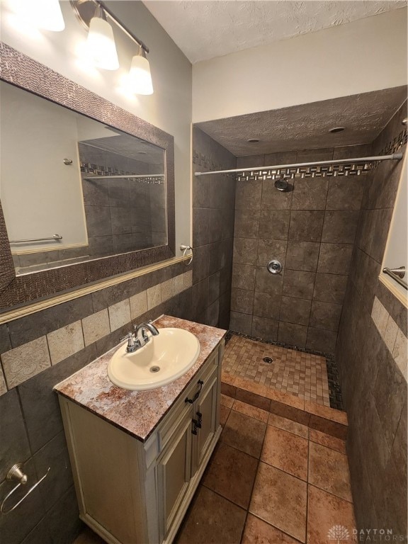 bathroom with tile patterned flooring, vanity, tiled shower, decorative backsplash, and tile walls