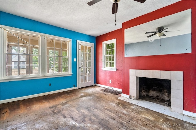 unfurnished living room featuring a textured ceiling, a tiled fireplace, hardwood / wood-style floors, and ceiling fan