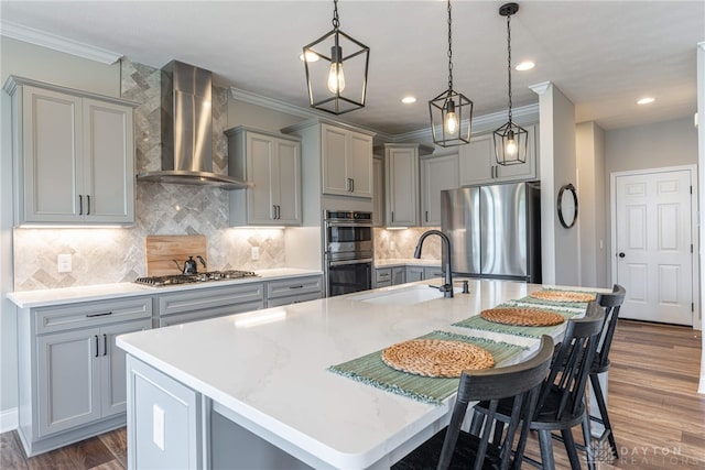 kitchen featuring a kitchen island with sink, hanging light fixtures, wall chimney exhaust hood, and stainless steel appliances