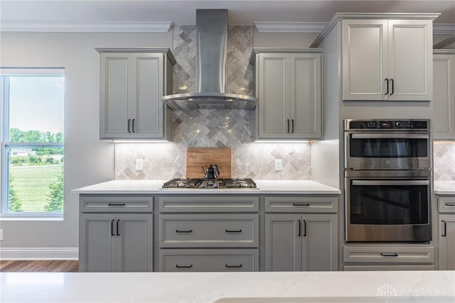 kitchen featuring stainless steel appliances, gray cabinets, crown molding, and wall chimney range hood