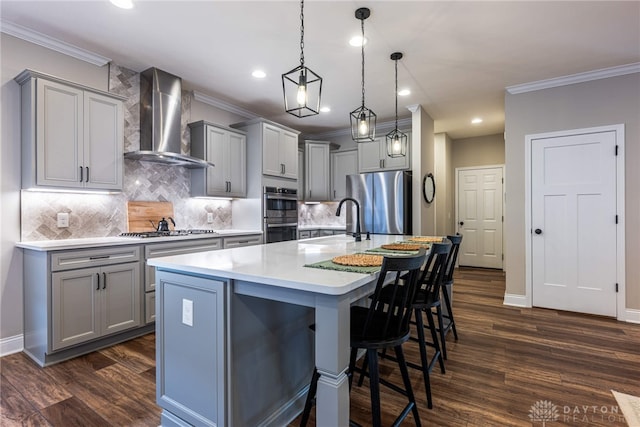 kitchen with stainless steel appliances, gray cabinetry, hanging light fixtures, and wall chimney range hood