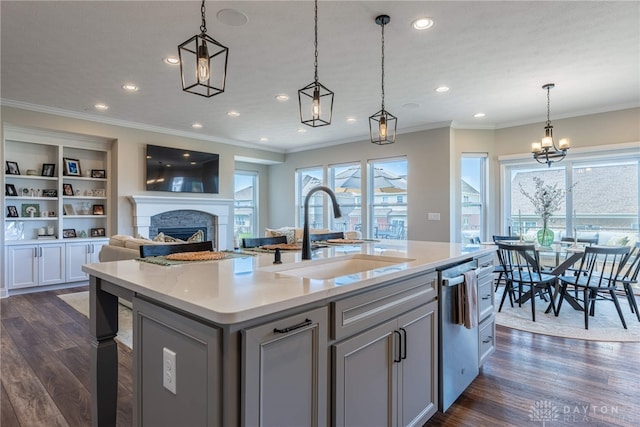 kitchen featuring sink, a stone fireplace, dark hardwood / wood-style floors, pendant lighting, and a kitchen island with sink