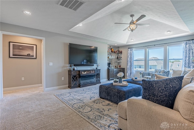 living room with a tray ceiling, ceiling fan, light carpet, and a textured ceiling