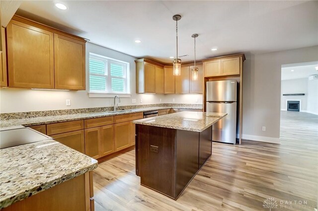 kitchen with sink, light hardwood / wood-style flooring, appliances with stainless steel finishes, light stone countertops, and decorative light fixtures