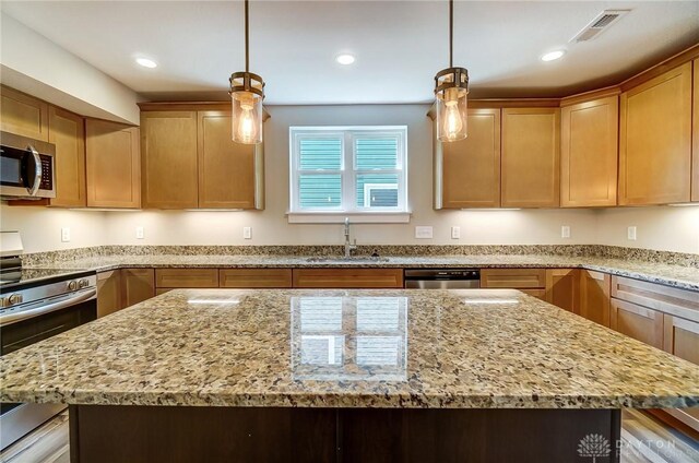 kitchen featuring sink, light stone counters, decorative light fixtures, appliances with stainless steel finishes, and a kitchen island