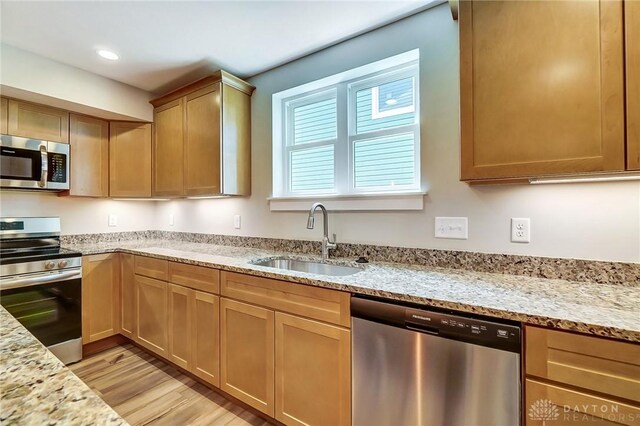 kitchen with appliances with stainless steel finishes, sink, light stone counters, and light hardwood / wood-style flooring