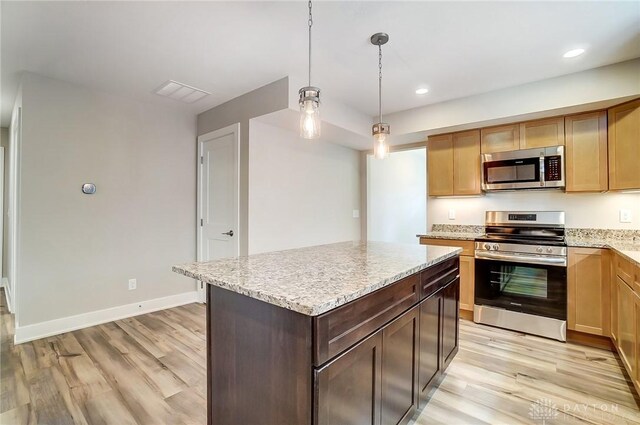 kitchen featuring a kitchen island, appliances with stainless steel finishes, hanging light fixtures, light stone countertops, and light hardwood / wood-style flooring