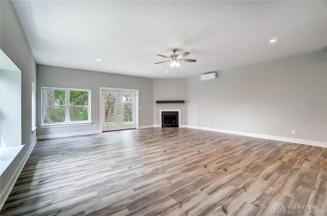 unfurnished living room featuring french doors, ceiling fan, a wall unit AC, and light hardwood / wood-style flooring