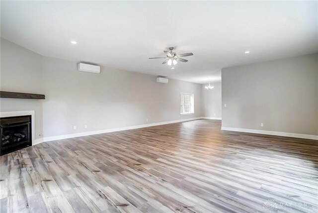 unfurnished living room featuring a wall mounted AC, ceiling fan with notable chandelier, and light wood-type flooring