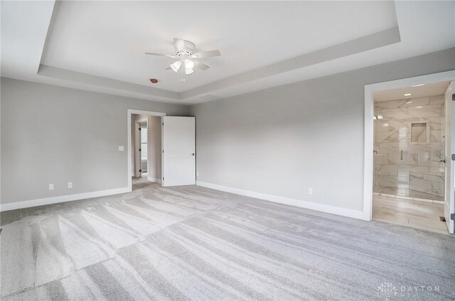 unfurnished room with a raised ceiling, light carpet, and ceiling fan