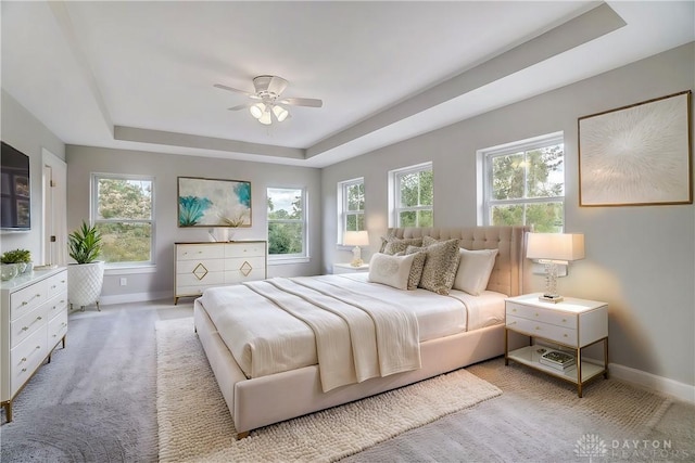 carpeted bedroom featuring multiple windows, a tray ceiling, and ceiling fan